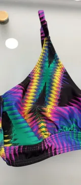 Conjunto de bikini con corpiño de triángulo sin aro, con estampado geométrico vibrante en tonos neón sobre fondo negro, y breteles ajustables. La parte inferior es una bombacha clásica de tiro alto, color negro liso.