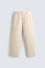 Pantalón chino de algodón color beige, de corte relajado (relaxed fit) y tiro medio. Presenta bolsillos delanteros y bolsillos traseros de vivo con cierre de cremallera y botón.