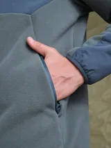 Campera de polar con cierre frontal completo, cuello alto y bolsillo en el pecho con cierre. Presenta un diseño combinado con paneles de tela técnica en la parte superior y polar en el resto de la prenda, con logo de la marca Benson & Thomas estampado en el hombro.