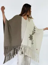 Ruana de punto bicolor, con un lado marrón y otro lado beige con detalle de bordado floral y flecos en los bordes inferiores.
