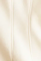 Buzo de felpa color beige con cuello redondo acanalado, mangas largas raglán y costuras moldeadoras en la cintura que crean una silueta entallada.