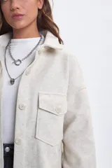 Sobrecamisa de paño en color beige, con cuello camisero, cierre frontal de botones y dos bolsillos delanteros con solapa. Presenta un corte holgado y mangas largas.