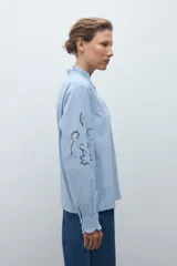Camisa blanca de manga larga con cuello alto fruncido y bordados calados en el pecho y los hombros.