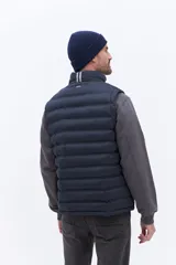 Chaleco puffer negro con diseño acolchado horizontal, cuello alto y cierre frontal. Presenta un bolsillo lateral con detalle de marca grabado.