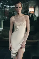Vestido midi de estilo lencero confeccionado en tejido satinado color beige. Presenta escote recto con tirantes finos y aplicaciones de encaje a tono en el escote y en el ruedo.