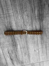 Cinto marrón de gamuza con tachas plateadas y hebilla metálica plateada.