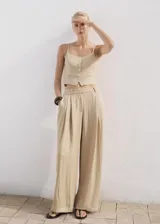 Chaleco tipo crop top de color beige, con tirantes finos, escote recto y cierre frontal de botonadura con botones revestidos. Cuenta con dos bolsillos de ribete delanteros y bajo con diseño asimétrico.
