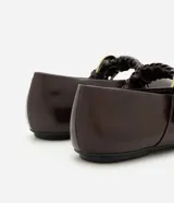 Chatitas de estilo bailarina en color marrón oscuro, confeccionadas en poliuretano. Presentan punta redondeada y una tira ajustable sobre el empeine con detalle de trenzado y hebilla metálica dorada.