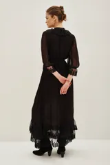 Vestido midi negro de estilo romántico, confeccionado en tejido semitransparente con detalles de encaje en el cuello, la cintura y el ruedo. Presenta mangas tres cuartos con terminación en encaje, escote en V con volados y un lazo de ajuste en la cintura.