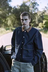 Campera de denim azul oscuro con cuello clásico marrón, cierre frontal con botones metálicos, bolsillos delanteros con solapa y puños con botones. Confeccionada en tejido denim resistente con estructura de sarga.