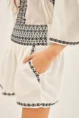 Conjunto de dos piezas compuesto por una blusa de manga tres cuartos y un short, ambos confeccionados en algodón color crudo con detalles de bordados geométricos en negro. La blusa presenta cuello redondo y el short cuenta con bolsillos laterales.