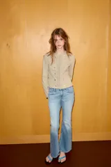 Chaqueta de cuello redondo y manga larga en color beige. Presenta un diseño con doble hilera de botones decorativos en el frente, detalles de encaje a tono y cierre frontal mediante ganchos metálicos ocultos.