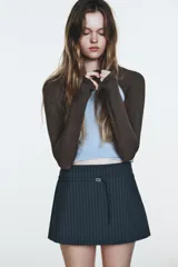 Falda pantalón (skort) de tiro medio, color azul grisáceo con finas rayas verticales blancas. Presenta un cinturón fino con hebilla metálica rectangular y cierre lateral oculto.