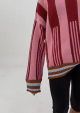 Buzo oversize de punto con cuello alto, mangas largas y diseño a rayas verticales en tonos rosa y bordó.