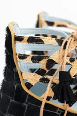 Botines bajos negros con diseño tejido y cordones con borlas. Presentan detalles de animal print en el tobillo y ribete ocre.