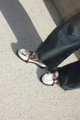Mocasín de estilo náutico confeccionado en cuero, combinando una base de cuero con textura de pelo en color negro y detalles de cuero con textura croco en color marrón. Presenta cordones decorativos con borlas laterales y suela plana de goma.