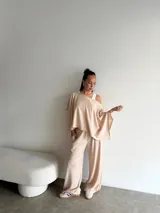 Conjunto de dos piezas compuesto por un top de corte asimétrico con escote amplio y mangas estilo capa, y un pantalón de corte recto y holgado. Ambas prendas están confeccionadas en tejido de lanilla gris.