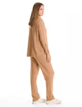 Buzo de tejido suave con cuello volcado ajustable mediante cordones con punteras metálicas. Presenta mangas largas con puños decorados con botones metálicos, hombros caídos y ruedo redondeado con aberturas laterales.