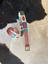 Cinturón de cuero en tono tostado con bordado a mano de hilos encerados en tonos marrones y beige con motivos geométricos, y hebilla metálica rectangular.