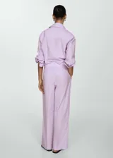Pantalón wide leg de tiro medio con diseño de rayas verticales finas en color lila. Presenta bolsillos laterales, bolsillos traseros de ribete, trabillas para cinturón y cierre frontal oculto con botón, gancho y cremallera.