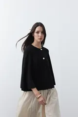 Saco tipo capa de punto color negro, con silueta fluida, corte amplio y cierre frontal con dos botones dorados.