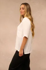 Blusa blanca de corte holgado con cuello redondo, mangas cortas con vuelta y un bolsillo aplicado en el pecho.