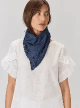 Bandana de jean azul con bordes deshilachados, pespuntes hechos a mano y pequeños apliques metálicos colgantes.