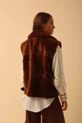 Chaleco de piel sintética en color chocolate, con cierre frontal y detalles de cuero en los bordes. Presenta un diseño de cuello solapa y ajuste lateral con hebillas.