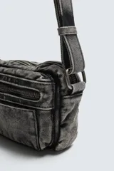 Bandolera de tejido denim con efecto lavado, cuenta con compartimento principal con cierre de cremallera, bolsillo interior con cierre y asa de hombro ajustable.