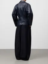 Chaqueta tipo biker de cuero sintético en color azul oscuro, con solapas, cierre frontal cruzado con cremallera, cintura entallada y mangas largas. Cuenta con bolsillos delanteros con cremallera invisible.