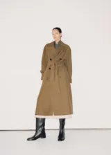 Trench coat de corte oversize y diseño largo en color verde oliva. Presenta cierre de doble botonadura, cuello con solapas de muesca, trabillas en hombros y mangas, y cinturón desmontable a tono. Incluye forro interior y abertura posterior en el bajo.