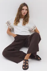 Blusa blanca de jersey con mangas cortas amplias de tela plana, decoradas con bordados geométricos en tonos marrón y azul marino.