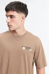 Remera oversize color marrón claro con estampado gráfico en la espalda que incluye frases como "Stay Original Forever", "All About Having Fun" y el logo de Mistral, junto con otros garabatos y stickers.