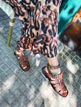 Sandalias planas de cuero color marrón, con tiras anchas y hebillas plateadas.