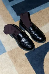 Mocasines negros de cuero vegano con suela gruesa y tira superior decorada con tachas metálicas doradas.