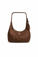 Cartera de formato amplio color marrón, confeccionada en poliéster, con silueta curva y caída suave. Presenta asa larga para llevar al hombro, cierre superior y pequeño aplique metálico en el frente.