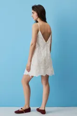 Vestido corto blanco de corte en A, confeccionado en tela con diseño de broderie floral y bordes scalloped. Cuenta con escote cuadrado y tirantes finos.