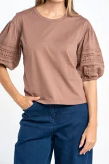 Remera negra de algodón con mangas cortas abullonadas que presentan detalles de encaje bordado y calado en los extremos.