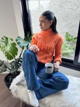 Polera elastizada color naranja con cuello alto y diseño trenzado.