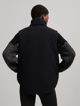 Chaleco negro capitoneado con cuello de piel sintética y cierre frontal con cremallera. Diseño sin mangas y corte recto.