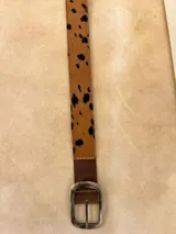 Cinturón de cuero con detalle de pelo vacuno estampado con manchas tipo animal print, hebilla metálica rectangular con logo grabado.