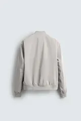 Cazadora bomber ligera de tejido técnico color verde oliva, con cuello, puños y bajo en rib elástico. Presenta cierre frontal de cremallera y bolsillos de vivo en la cadera.