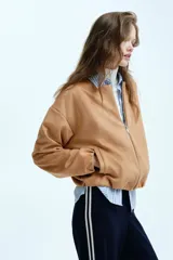 Chaqueta de punto pesado color tostado, con escote redondo, cierre frontal y bolsillos laterales. Presenta un diseño oversized con hombros caídos y terminaciones elásticas en puños y bajo.