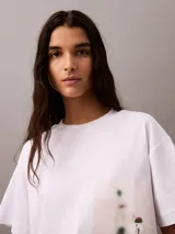 Remera blanca de algodón con corte cropped y mangas cortas. Presenta un estampado fotográfico floral de Calvin Klein en el lateral.