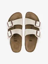 Sandalia Birkenstock modelo Arizona de dos tiras, color blanco nacarado brillante. Presenta hebillas ajustables de metal color cobre y plantilla anatómica de corcho-látex forrada en ante.