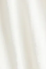 Vestido corto de color blanco en tejido con textura, con escote redondo, abertura con tiras para anudar, mangas largas abullonadas y falda de volados escalonados.