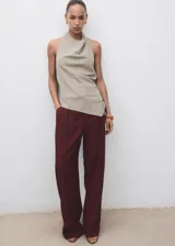 Top color beige, con cuello drapeado, diseño sin mangas, espalda abierta con cierre de lazo y dobladillo asimétrico.