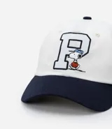 Gorra blanca de sarga con visera azul marino y bordado de Snoopy jugando baseball.