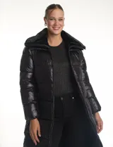 Campera puffer larga de acabado satinado con diseño capitoneado horizontal. Presenta un amplio cuello envolvente revestido en piel sintética, cierre frontal bidireccional y bolsillos laterales con cremallera. Incluye logo metálico en la manga.