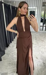 Vestido largo color marrón, con escote profundo en V, cuello halter y falda con tajo lateral. Presenta un diseño drapeado en la cintura.